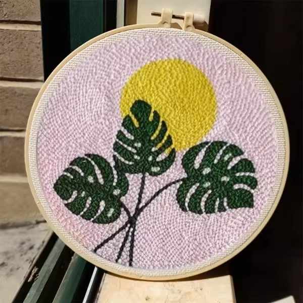 CraftHoop punch needle embroidery kit featuring a leaf and abstract design in green, beige, and orange tones, displayed on a white surface.