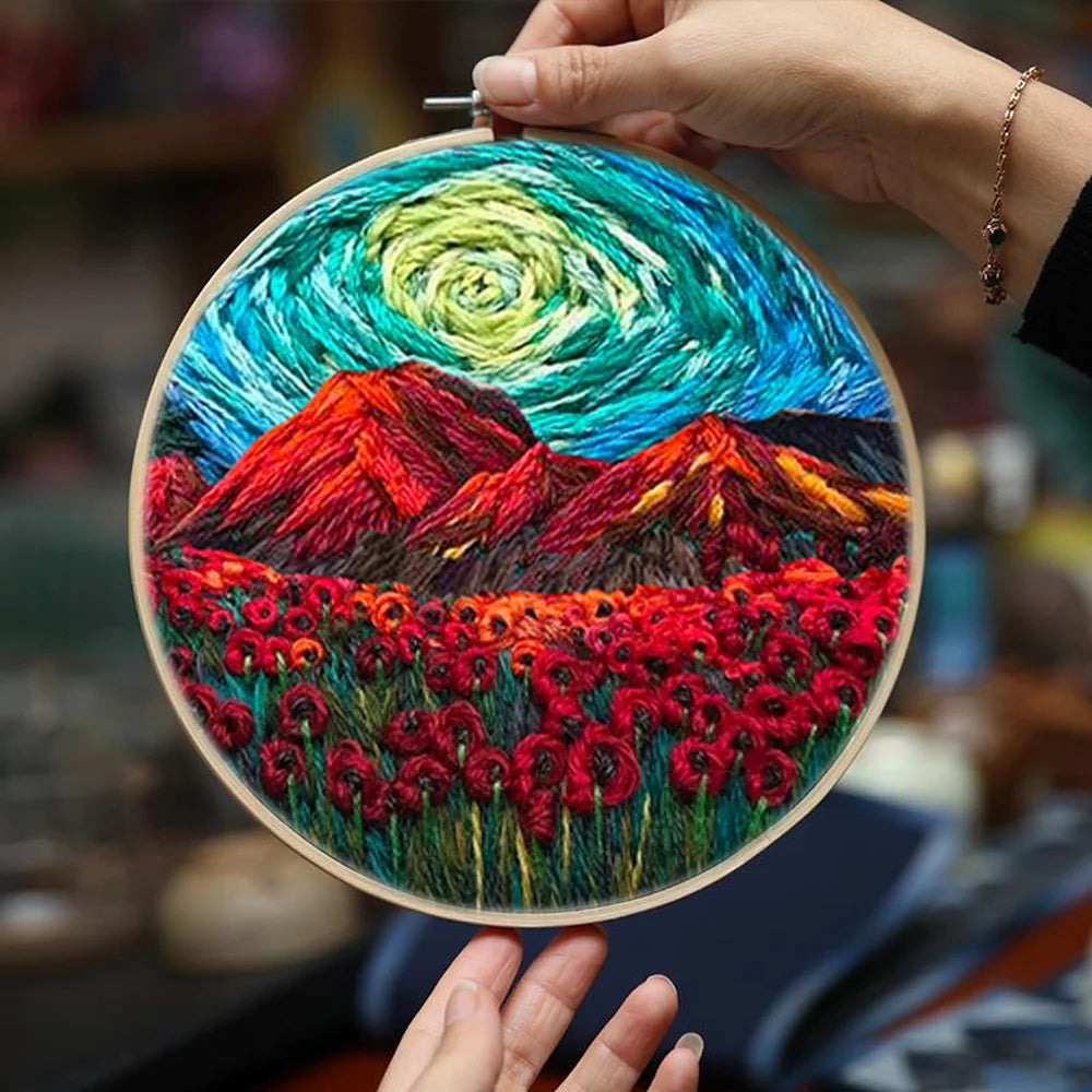 CraftHoop embroidery kit featuring a vibrant landscape design with red mountains, swirling sky, and a field of poppies on fabric, displayed on a wooden surface