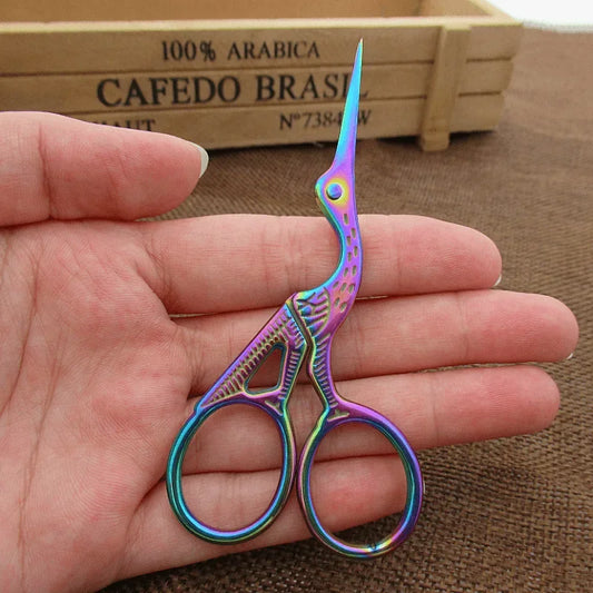 Close-up of rainbow-colored stork embroidery scissors, displayed on a wooden surface, showcasing their intricate design and sharp blades