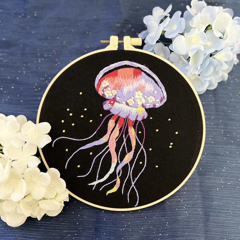 CraftHoop jellyfish embroidery kit featuring a vibrant green and blue jellyfish design on black fabric, displayed on a wooden stand