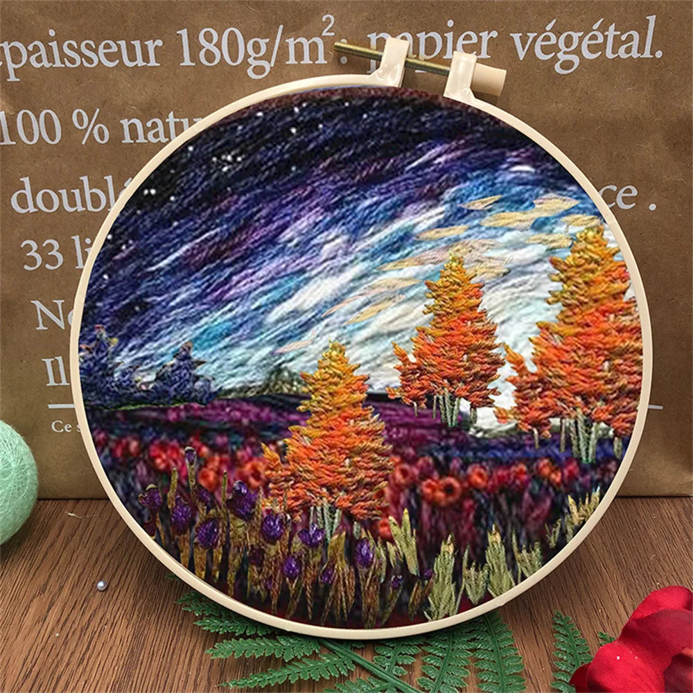 CraftHoop landscape embroidery kit featuring a sunset design with mountains and trees, displayed on a wooden surface with decorative leaves