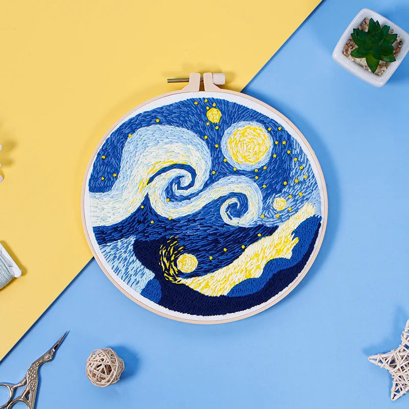 Close-up of CraftHoop starry night embroidery kit with a detailed swirling sky design on blue fabric, displayed on a yellow and blue surface