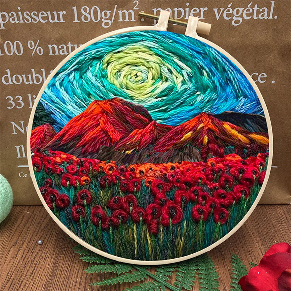 CraftHoop landscape embroidery kit with a vibrant mountain scene and colorful sky, displayed on a wooden surface with decorative elements