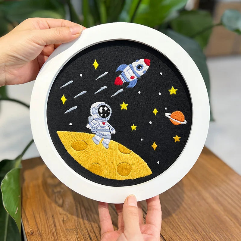 Finished CraftHoop Little Astronaut Embroidery Kit displayed on a wooden stand featuring an astronaut and planets.