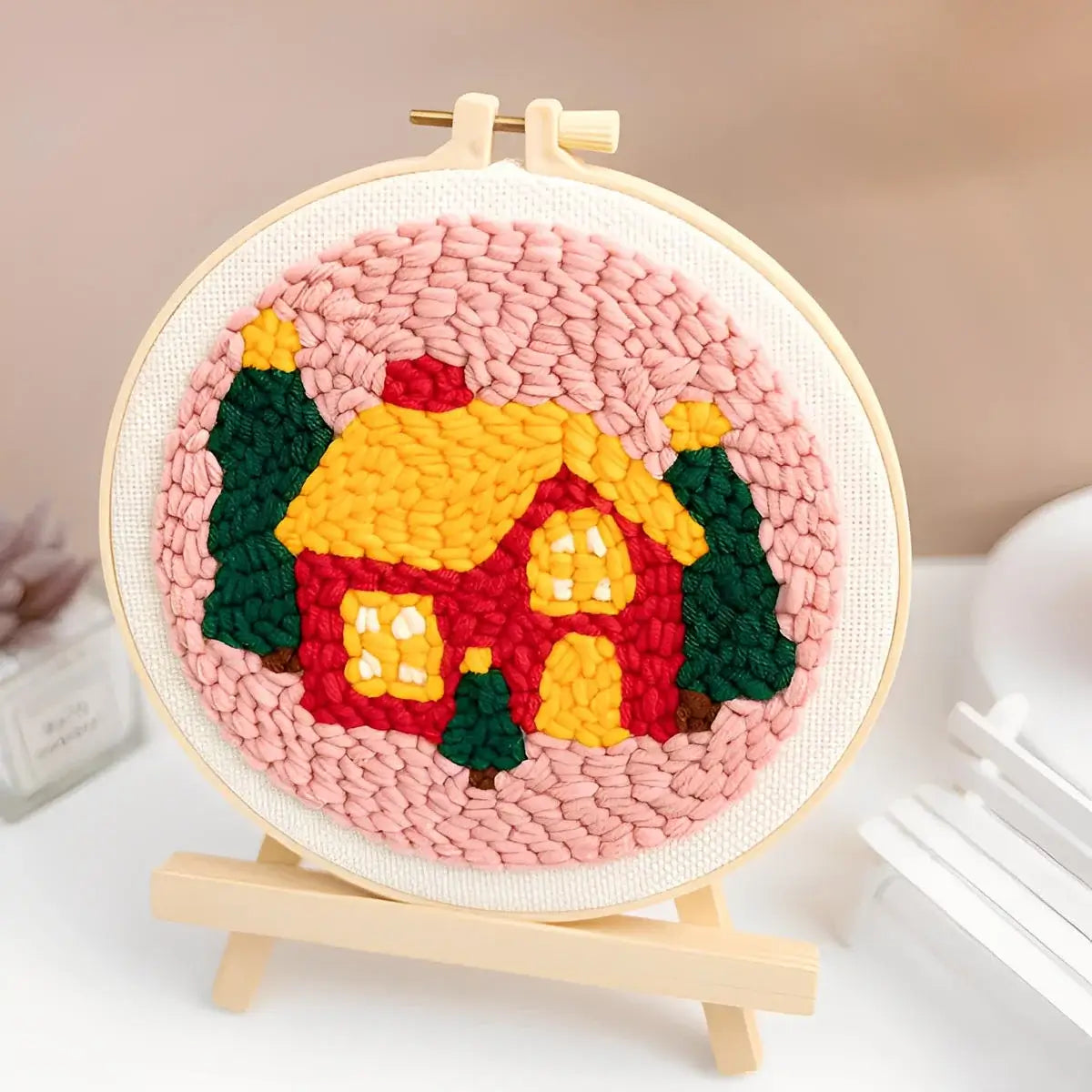 CraftHoop Christmas Cheer Punch Needle Kit featuring a colorful holiday home design with trees and pink background.