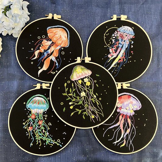 CraftHoop embroidery kit featuring a colorful jellyfish design on black fabric, displayed on a wooden stand with white flowers