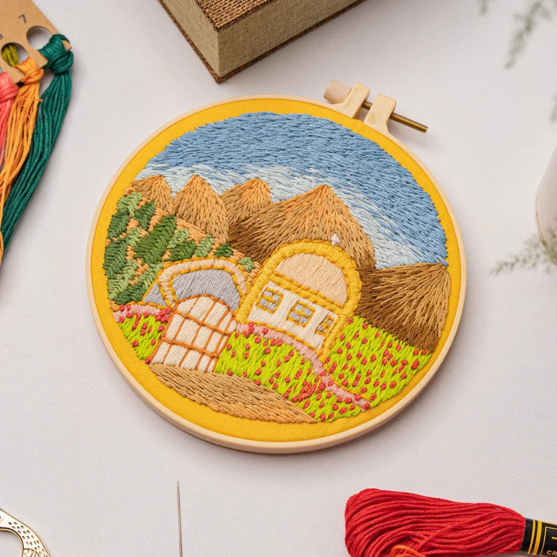 Collection of landscape-themed embroidery kits from CraftHoop, featuring mountains, rivers, and sunsets, displayed on an open magazine with embroidery threads