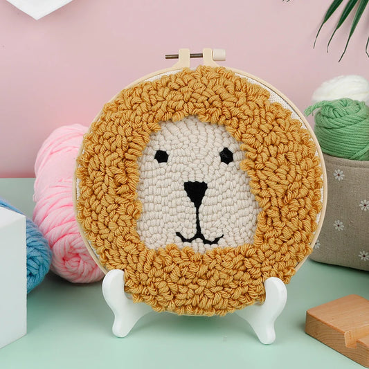 CraftHoop punch needle embroidery kit featuring a cute lion design with a fluffy mane, displayed on a white stand with yarn in the background.