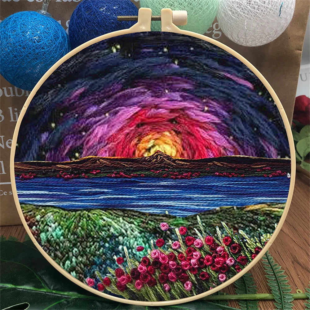 CraftHoop landscape embroidery kit featuring a twilight mountain scene with swirling sky and a field of flowers, displayed on a wooden surface