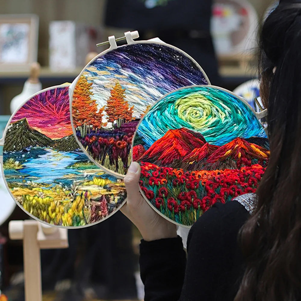 Collection of landscape-themed embroidery kits from CraftHoop, showcasing various colorful designs, including mountains, trees, and skies, held in hands