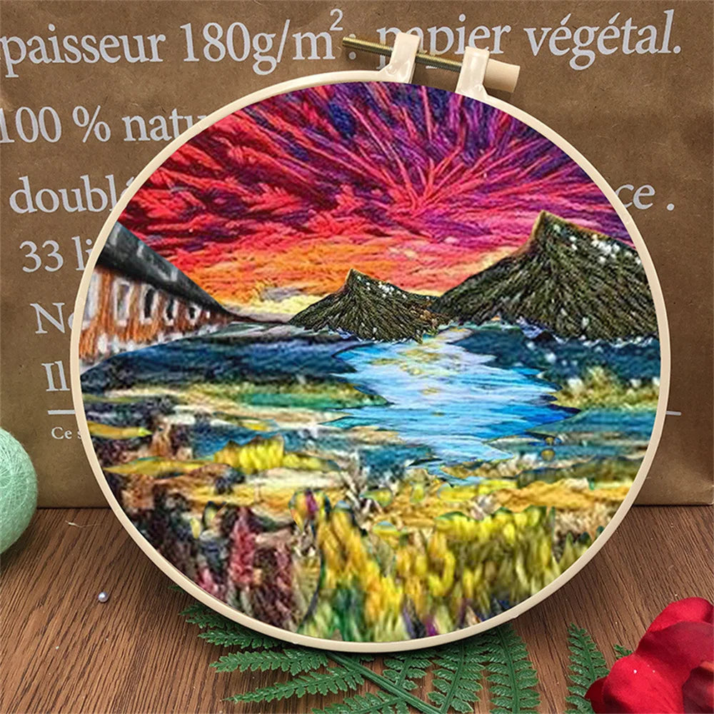 Close-up of CraftHoop embroidery kit with a detailed landscape design of mountains, sky, and a field of poppies, displayed on a wooden surface