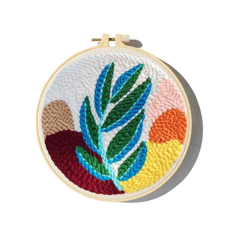 CraftHoop punch needle embroidery kit with a tropical leaf design and yellow sun on purple fabric, displayed near a window.