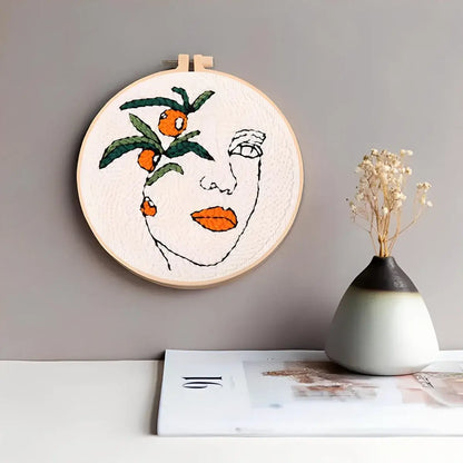CraftHoop Botanical Muse Punch Needle Kit showcasing a face design with greenery and citrus details in an embroidery hoop.