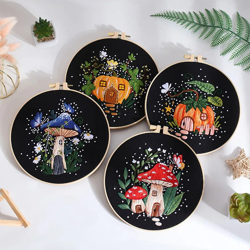 Three mushroom-themed embroidery kits from CraftHoop, including pumpkin, toadstool, and mushroom house designs, displayed on a white surface with decorative elements