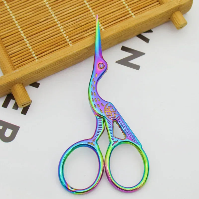 Hand holding rainbow-colored stork embroidery scissors, highlighting the small size and ergonomic design, perfect for precise cuts